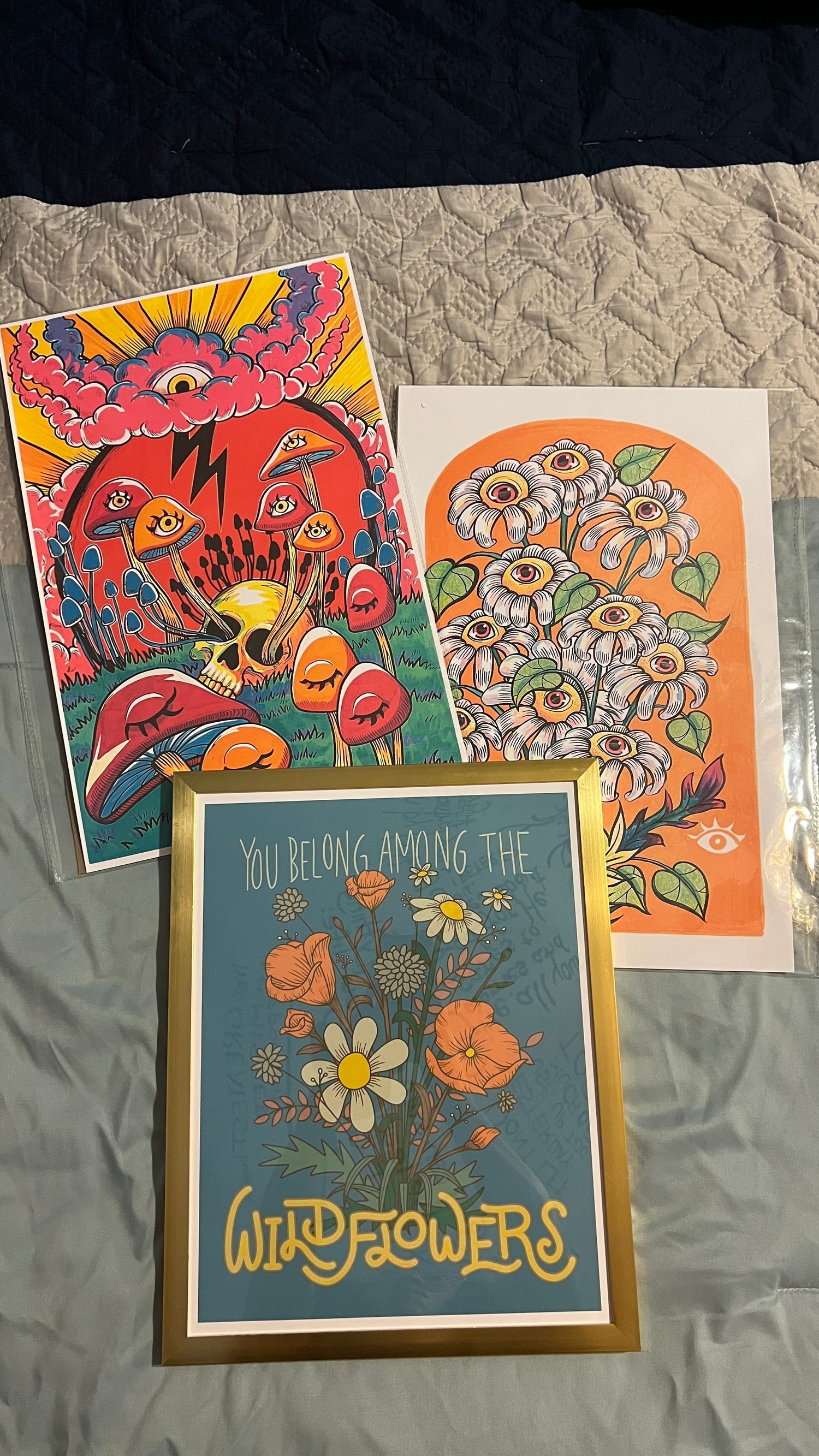 Three colorful poster-sized prints of mushrooms and flowers with eyes